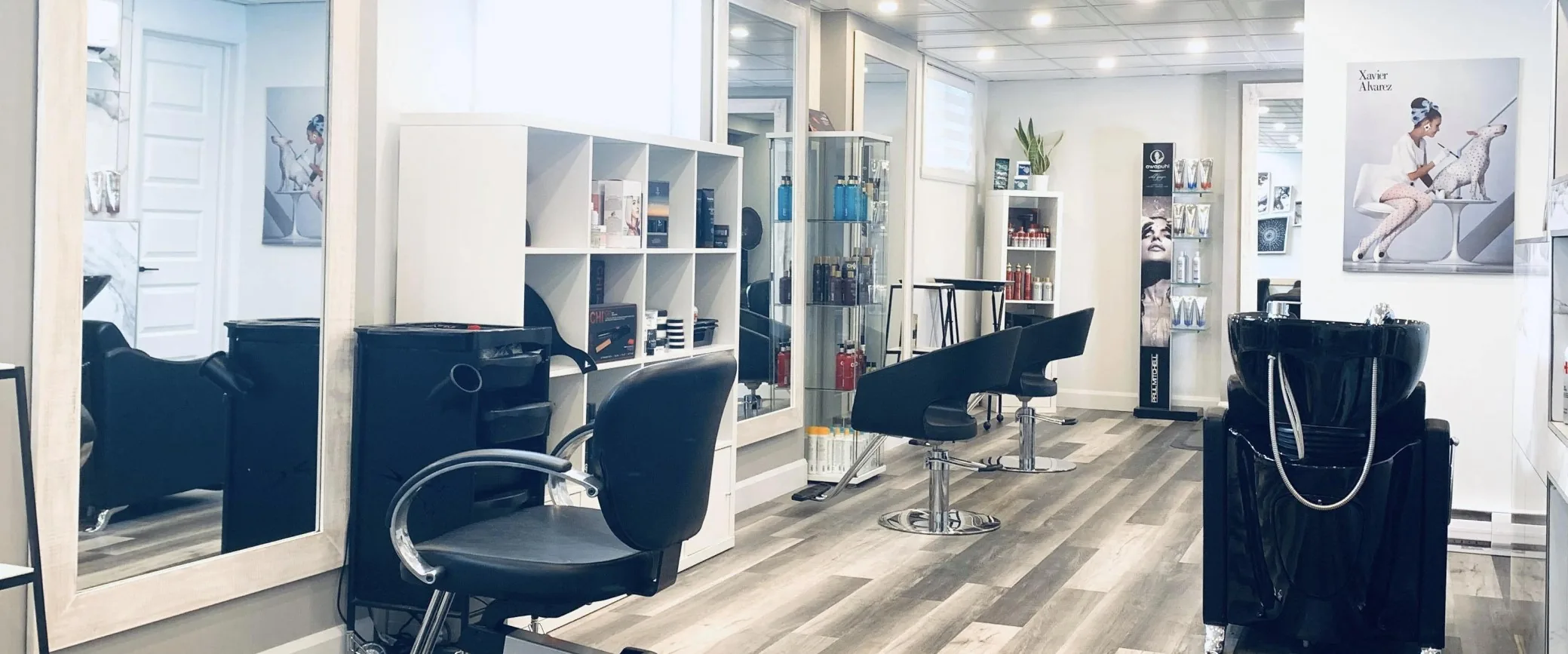 L’intérieur du salon : grands miroirs, fauteuils noirs, étagères de produits et bac à shampoing